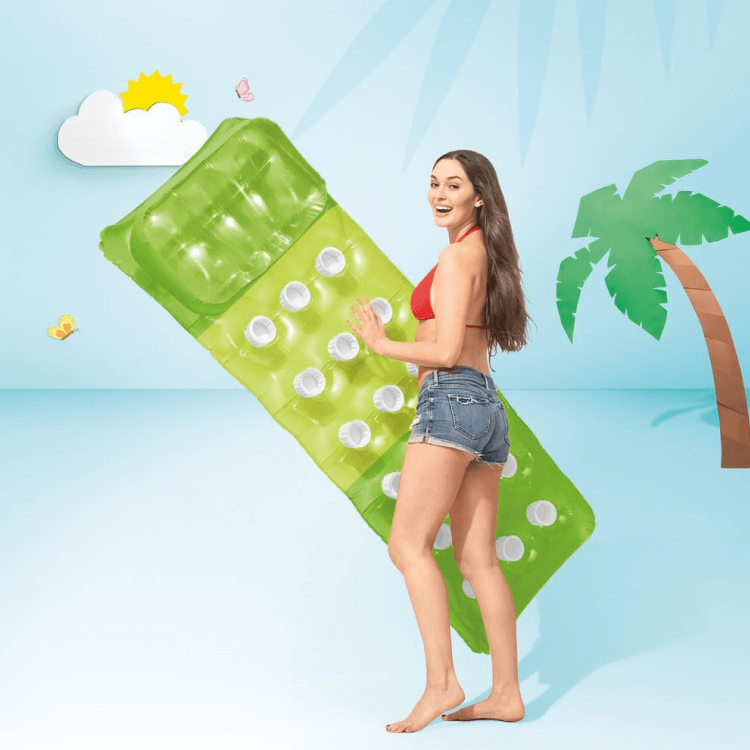 A woman holding a bright green Intex 18-pocket pool lounge float against a light blue summer background.